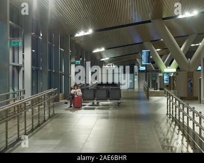 Donna con valigia rosso è seduta nel vuoto nella sala di attesa di un aeroporto. Aeroporto di Platov, Rostov-on-Don, in Russia Foto Stock