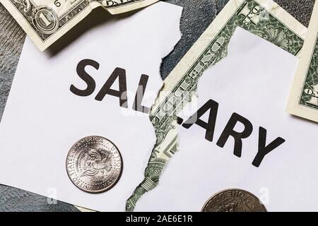 Un foglio di carta bianca con le parole lo stipendio, strappata a metà. A basso salario. Monete degli Stati Uniti d'America sul tavolo Foto Stock