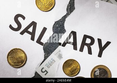 Un foglio di carta bianca con le parole lo stipendio, strappata a metà. A basso salario. Monete metalliche in euro sul tavolo Foto Stock