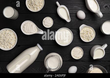 Diversi tipi di prodotti lattiero-caseari sul nero lo sfondo di legno, set di latte, ricotta, panna acida e lo yogurt, vista dall'alto Foto Stock