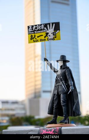 Un esempio dell'arte di protesta di Hong Kong trovata in molti mezzi di comunicazione attraverso la città. Una bambola di V da V per vendetta tiene un banner di protesta. Centro Di Hong Kong 7 Dicembre 2019, Foto Stock