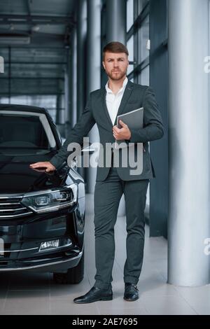 Foto verticale. Moderno ed elegante imprenditore barbuto nel salone automobilistico Foto Stock