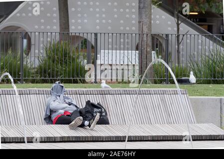 In massa le fontane di acqua schizzare in aria mentre una persona si siede al sole su un sedile di grandi dimensioni con il viso coperto in Sydney Darling Parco di quartiere Foto Stock