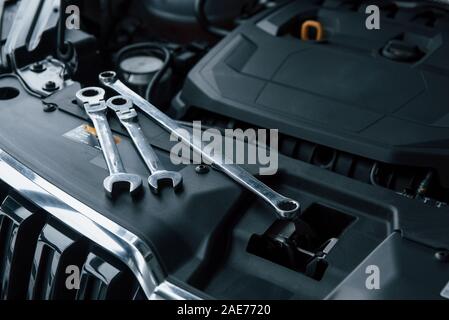 Colore nero interno. Strumenti di riparazione sdraiato sul motore di automobile sotto il cofano Foto Stock
