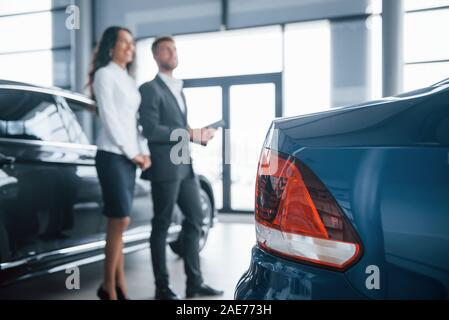 Parte posteriore del dipinto di blu car. Femmina e del cliente moderno ed elegante imprenditore barbuto nel salone automobilistico Foto Stock