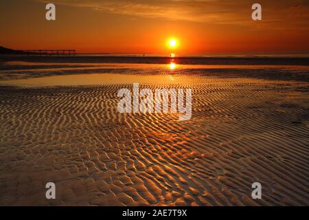 Il tramonto sul mare con una silhouette di un molo e modelli di sabbia a Saltburn dal mare, North Yorkshire, Inghilterra, Regno Unito. Foto Stock