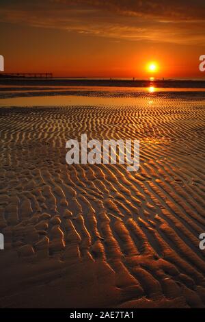 Il tramonto sul mare con una silhouette di un molo e modelli di sabbia a Saltburn dal mare, North Yorkshire, Inghilterra, Regno Unito Foto Stock