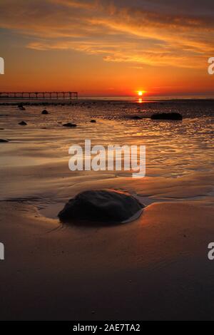 Il tramonto sul mare con una silhouette di un molo e modelli di sabbia a Saltburn dal mare, North Yorkshire, Inghilterra, Regno Unito Foto Stock