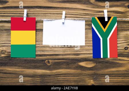 Appendere bandiere di Guinea e Sud Africa attaccata alla corda con vestiti perni con copia spazio bianco sulla nota carta su sfondo di legno.Diplomatic relativi Foto Stock