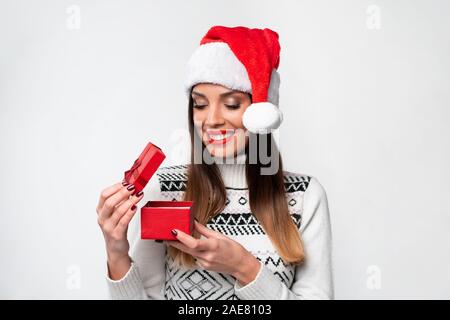 Close up ritratto bellissime caucasian woman in red Santa hat su bianco di sfondo per studio. Natale Anno Nuovo Concetto di vacanza sorpreso ragazza carina denti Foto Stock