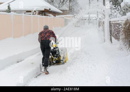 Uomo di funzionamento del ventilatore di neve per rimuovere la neve sul vialetto. Uomo che utilizza un spalaneve. Un uomo che pulisce la neve da marciapiedi con spalaneve. Foto Stock