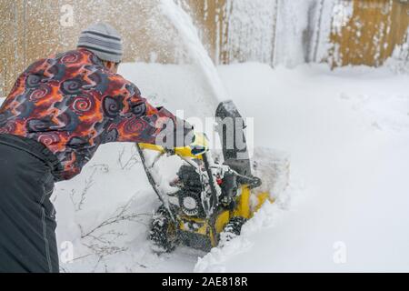 Uomo di funzionamento del ventilatore di neve per rimuovere la neve sul vialetto. Uomo che utilizza un spalaneve. Un uomo che pulisce la neve da marciapiedi con spalaneve. Foto Stock