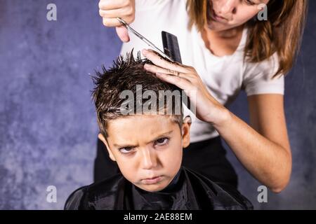 Bel ragazzo di ottenere un taglio di capelli con le forbici Foto Stock