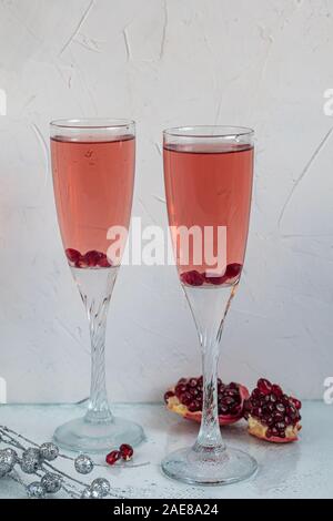 Holiday melograno drink. Vino di colore rosa. Sullo sfondo sono fette di melograno. Sfondo bianco. Champagne. Nuovo anno. Natale. Primo piano. Foto Stock
