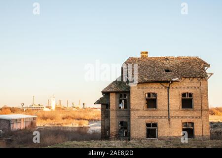 Abbandonato casa di fronte vecchie fabbriche e i magazzini con i loro caratteristici camini in Europa Orientale, in Pancevo, Serbia, Ex Jugoslavia, durante una Foto Stock