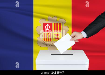Elezioni ad Andorra. La mano dell'uomo che mette il suo voto nella cassa di voto. Bandiera di Andorra sventolata sullo sfondo. Foto Stock