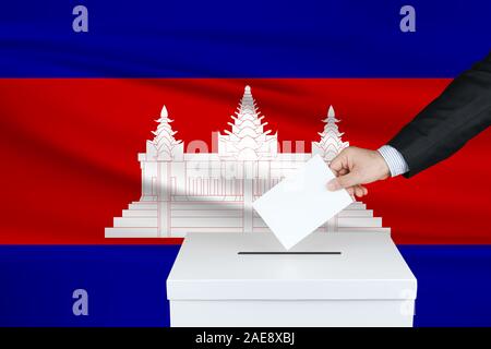 Elezioni in Cambogia. La mano dell'uomo che mette il suo voto nella cassa di voto. Bandiera Cambogia ondulato sullo sfondo. Foto Stock