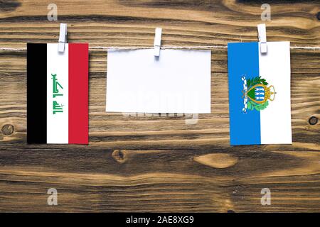Appendere bandiere di Iraq e San Marino attaccata alla corda con vestiti perni con copia spazio bianco sulla nota carta su sfondo di legno.Le relazioni diplomatiche Foto Stock