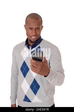 Un giovane arrabbiato americano africano uomo in piedi in un maglione con il suo telefono cellulare in mano confuso ciò che vede, isolato per sfondo bianco Foto Stock