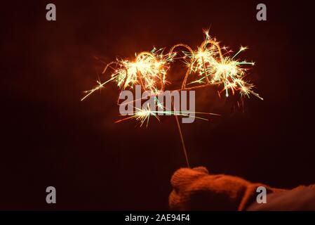 Mano umana con guanto tenendo un accensione 2020 Sparkler sagomata, all'esterno di notte Foto Stock