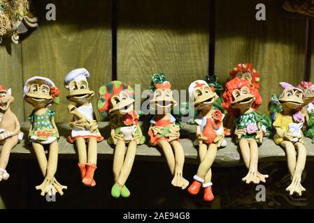 Ripiano sitter decor e figurine -- un gruppo di ceramiche colorate divertenti ragazza sorridente rane, molte forme diverse di argilla caratteri di donna seduta su uno scaffale di legno Foto Stock