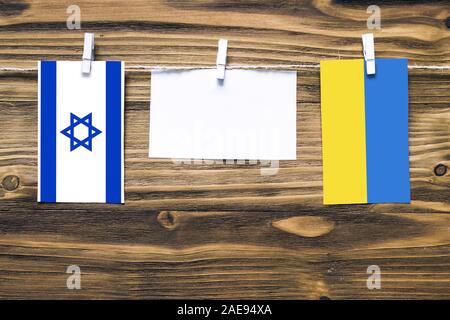 Appendere le bandiere di Israele e Ucraina attaccata alla corda con vestiti perni con copia spazio bianco sulla nota carta su sfondo di legno.Le relazioni diplomatiche b Foto Stock