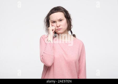 Riflessivo focalizzata giovane donna in abiti rosa con look accattivante cerca di ricordare qualcosa in mente. Studio shot Foto Stock