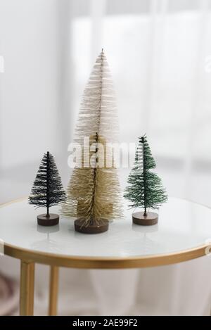 Piccoli alberi di Natale realizzati in bianco, Golden, verde il floccaggio fili su un vetro bianco tavolo. Sfondo elegante, parte di una moderna e luminosa decorazioni di Natale. Foto Stock