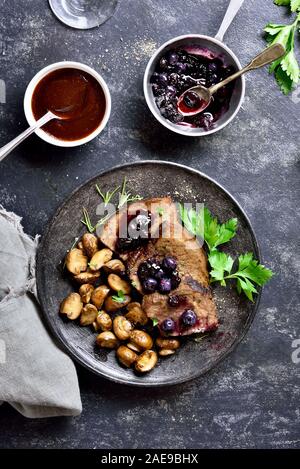 Slow manzo cotto con funghi e salsa di mirtilli sulla pietra scuro dello sfondo. Saporiti stufati di carne con funghi e salsa dolce. Vista superiore, laici piatta Foto Stock