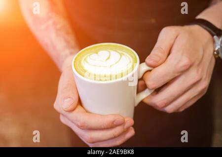 Barista maschio coppa di ritegno del matcha latte in mani. Alimentato alla moda di tendenza di tè dal Giappone Foto Stock