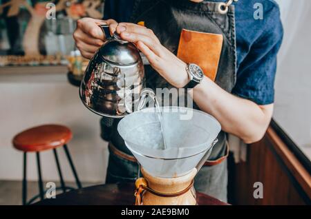 Mano versando acqua calda dal bollitore sopra la polvere di caffè. Barista maschio versando acqua bollente dal bollitore Foto Stock