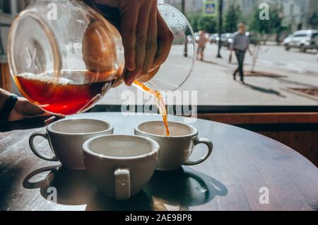 Barista versando il caffè dalla chemex alla ceramica tazza bianca. Caffetteria e terrazza Foto Stock