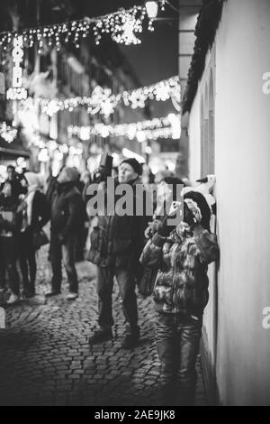 Strasburgo, Francia - Dic 20, 2016: francese street con la donna prendendo fotografia sullo smartphone della movimentata Rue du Maroquin decorate luminarie bokeh di fondo per il Mercato di Natale Foto Stock