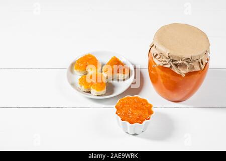 In casa la carota inceppamento in un vasetto di vetro e ciotola su un bianco sullo sfondo di legno. Deliziosi toast a forma di cuore con la carota marmellata. Copia dello spazio. Foto Stock