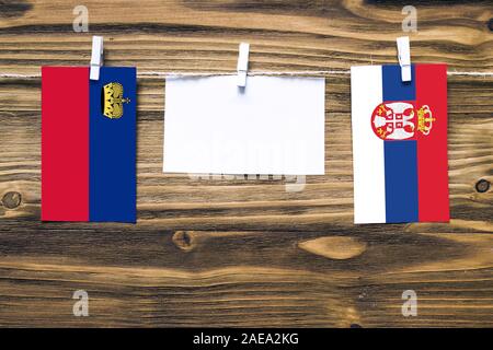 Appendere bandiere di Liechtenstein e la Serbia attaccata alla corda con vestiti perni con copia spazio bianco sulla nota carta su sfondo di legno.relat diplomatica Foto Stock