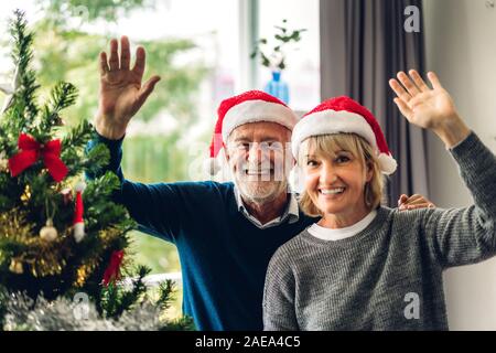 Ritratto di felice coppia senior in cappelli di Babbo Natale avendo divertimento sorridente in telecamera gesticolando e dire ciao a voi e godendo di trascorrere del tempo insieme a Chris Foto Stock