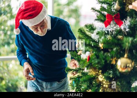 Senior rilassante uomo decorare albero di natale e sorridenti mentre festeggia capodanno e godendo di trascorrere del tempo insieme nel tempo di Natale a hom Foto Stock