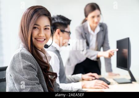 I giovani adulti cordiale e fiducia operatore agente donna sorridente con auricolari a lavorare in un call center con il suo collega di lavoro in team come cliente se Foto Stock