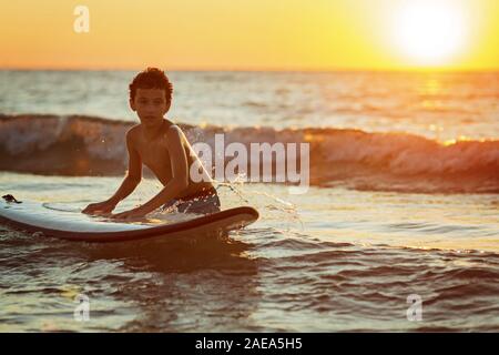 Ragazzo surfer ottenere pronto per la corsa sull'oceano onda contro la bellissima luce sinset Foto Stock