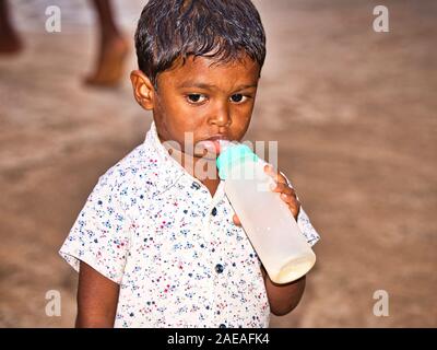 PUDUCHERRY, INDIA - dicembre circa, 2018. Unidentified timido giovani indiani dalit boy da sola per la strada del villaggio, bere il biberon con tristi e sh Foto Stock