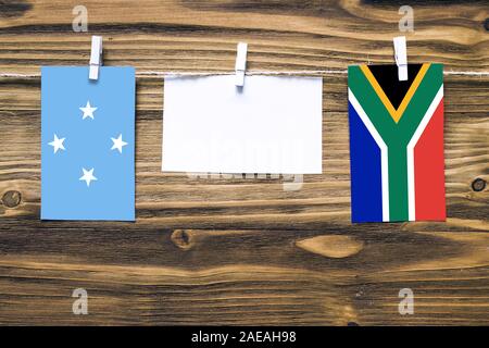Appendere bandiere della Micronesia e Sud Africa attaccata alla corda con vestiti perni con copia spazio bianco sulla nota carta su sfondo di legno.re diplomatica Foto Stock