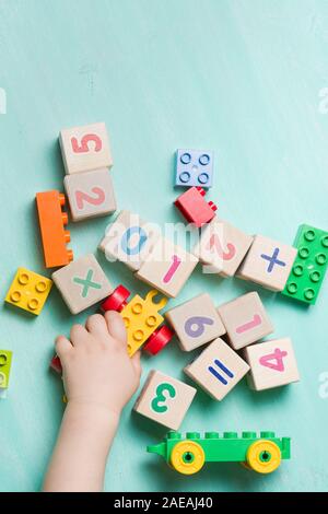 Bambini che giocano con i cubi di legno con numeri e colorati mattoni giocattolo su un turchese sullo sfondo di legno. Il Toddler numeri di apprendimento. La mano di un bambino takin Foto Stock