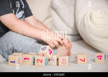 Bambini che giocano con i cubi di legno con i numeri. Il Toddler numeri di apprendimento. La mano di un bambino tenuto giocattoli. Ragazzo sul divano di casa, in interni. L'istruzione e l Foto Stock