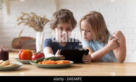 Bambini in età prescolare seduti a tavola in cucina utilizzando computer tablet Foto Stock