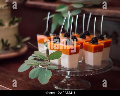 Giallo e Bianco dessert di gel con more decorate con rami di eucalipto e con cucchiai in loro Foto Stock