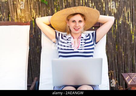 Ritratto di attraente soddisfatti i giovani adulti imprenditrice nel cappello e vestito seduto e in appoggio sul comodo divano letto con il computer portatile e di lavoro on-line. Lifesty Foto Stock