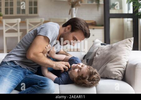 Padre solletica adorabile figlio divertendosi in salotto Foto Stock