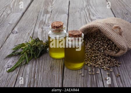 Sementi di canapa in un sacco di olio in un recipiente di vetro, foglie di cannabis sul tavolo di legno Foto Stock