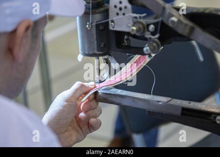 Le mani di un vecchio e un lavoratore con esperienza nella calzatura artigianali industria, eseguendo operazioni di cucitura su un pezzo di pelle vera, su un cuoio cucito machi Foto Stock