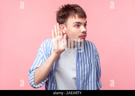 Ritratto di curiosi attenti i capelli castani uomo con piccola barba e baffi in casual striped shirt mantenendo la mano vicino a orecchio, ascoltando rumor, segreto Foto Stock